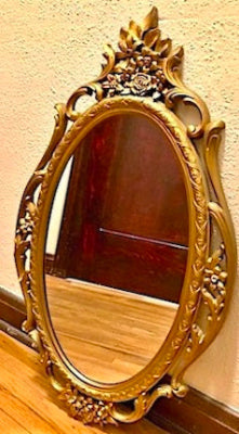 A vintage ornate gold wall-mounted mirror with floral patterns and a scalloped frame.
